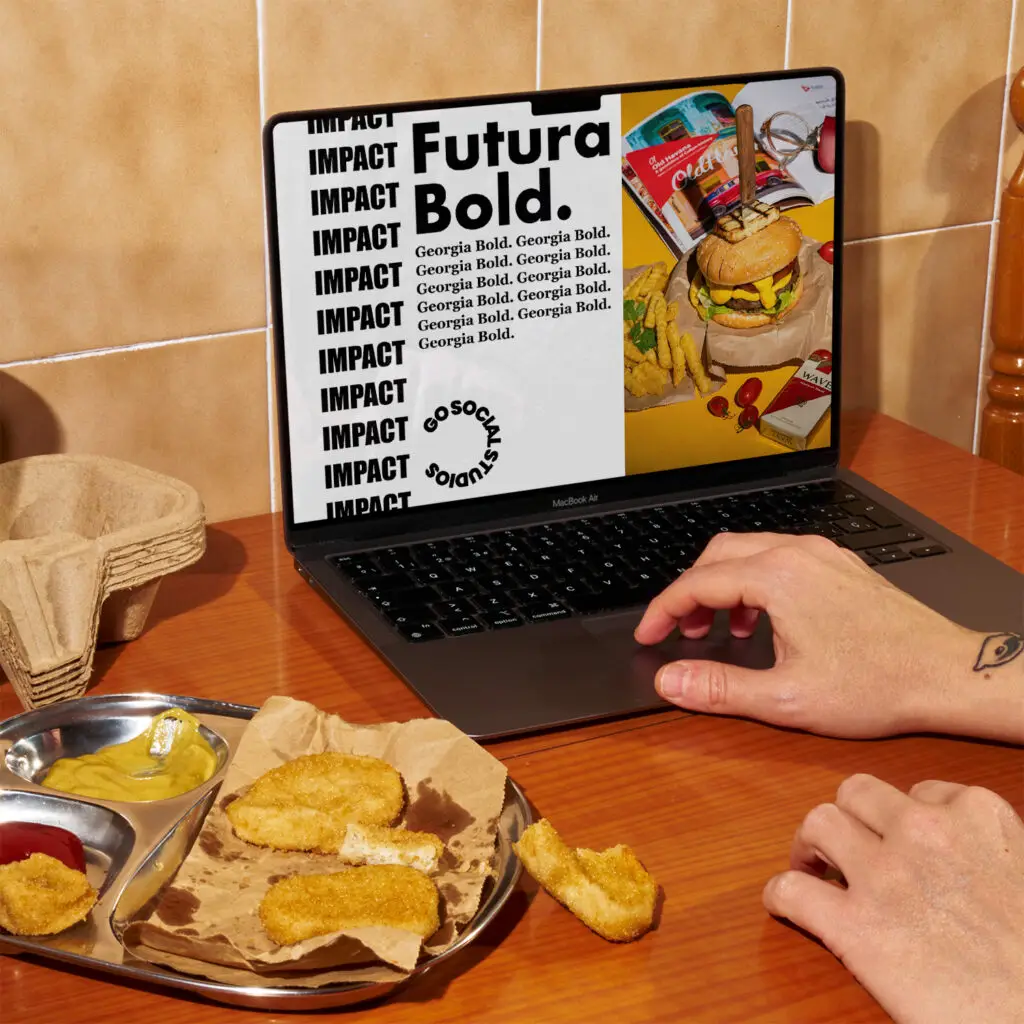 Laptop showing a branding design with fonts and packaging visuals, placed next to a food tray with fried snacks — Go Social Studios branding service showcase.